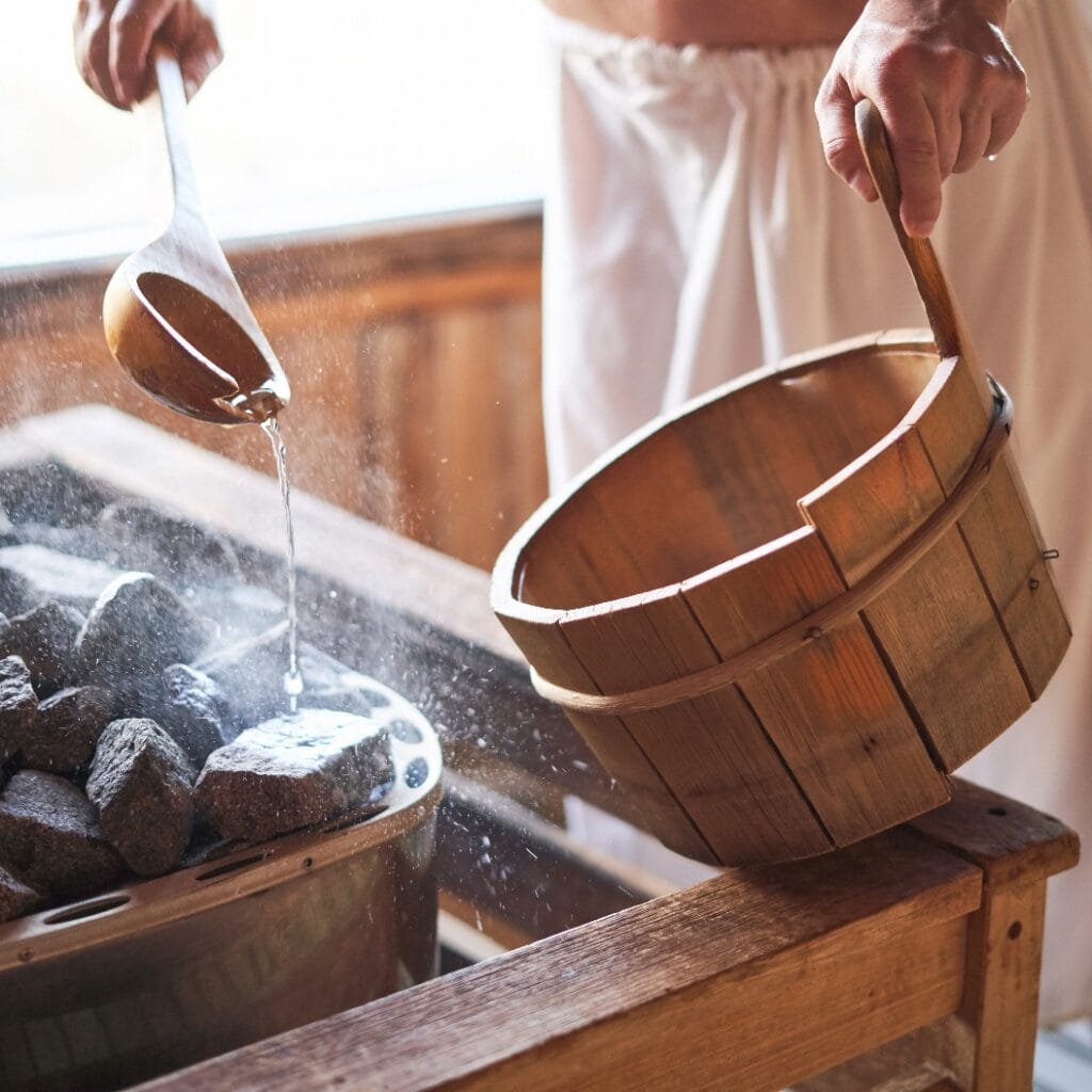 Man pouring water into hot stone in sauna room.