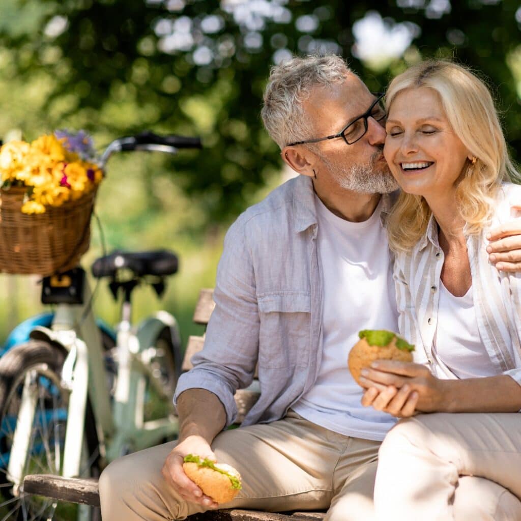 Senior Couple Having Lunch Break Outdoors While Sitting On Bench In Park