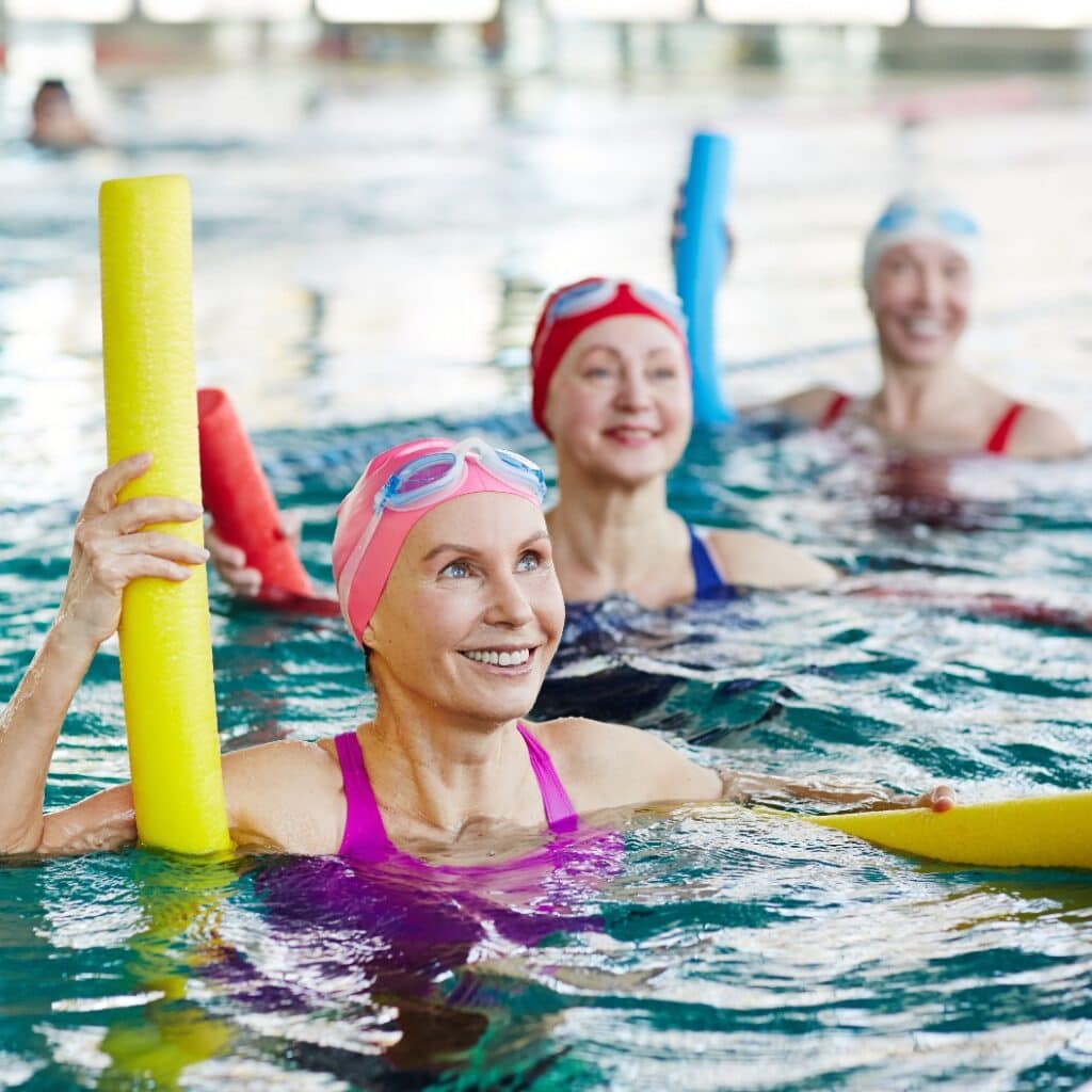 Smiling mature female in swimwear and two more active women listening to trainer advice during gymnastics in water