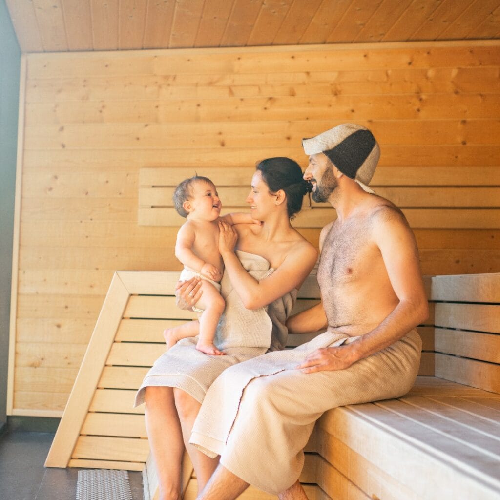 Young family resting with a little baby boy in sauna. Family vacation with one year child in spa