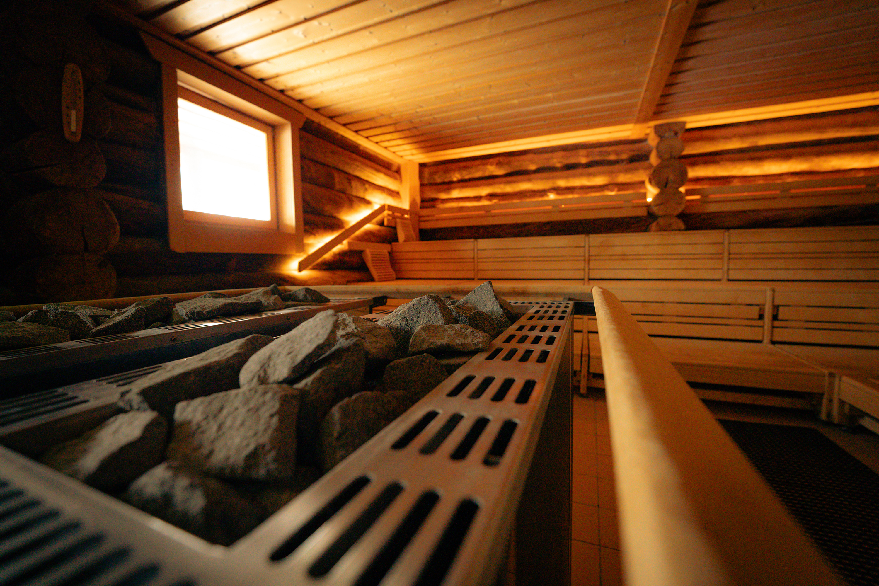 Ein leerer Saunaraum mit Holzbänken und Steinen auf einem Ofen.