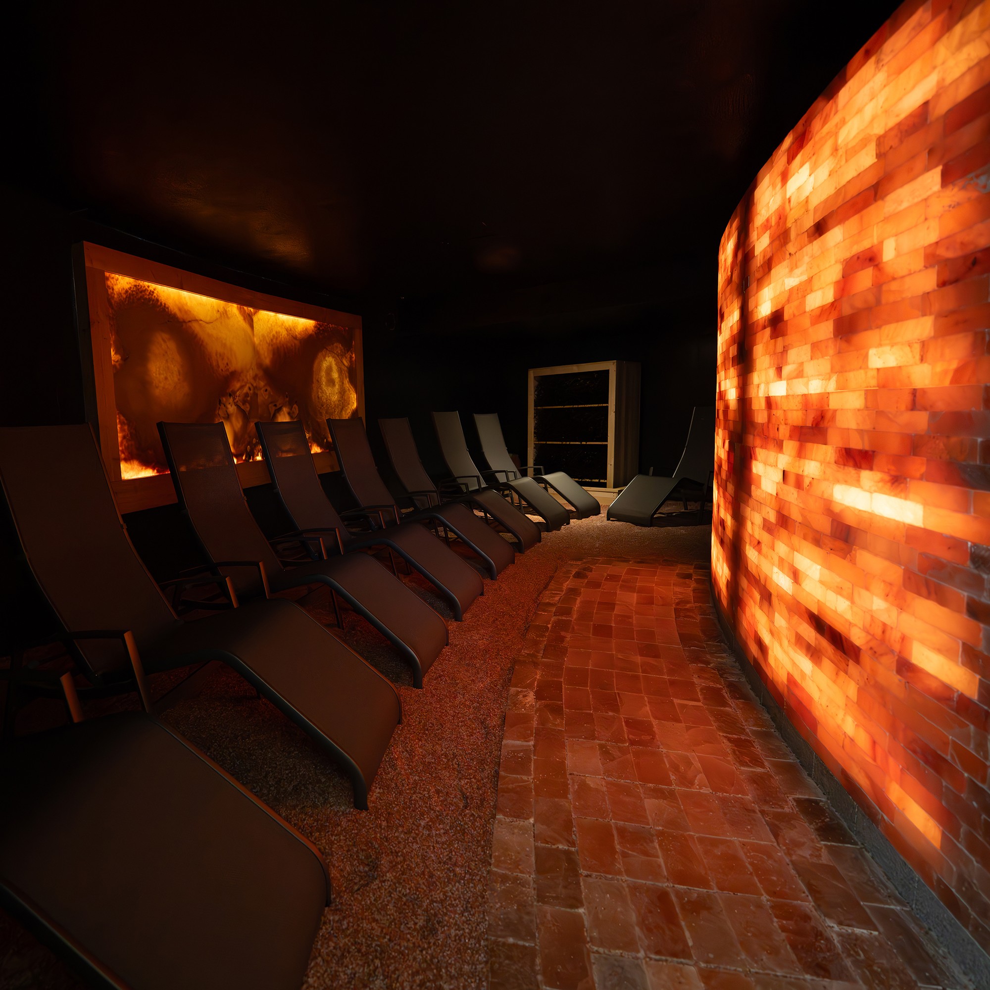 Ein dunkler Raum mit leeren Liegestühlen und einer beleuchteten Salzwand.