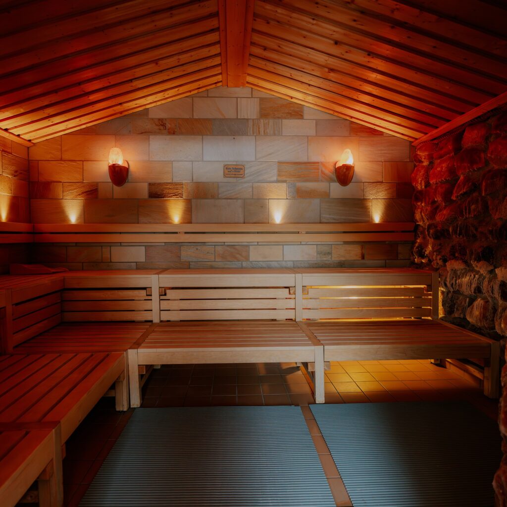 Holzsauna mit warmem Licht, Holzbänken und Steinwänden; einladende Atmosphäre.